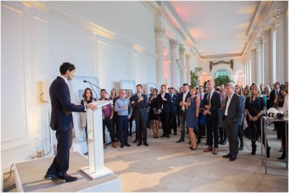 A person delivers a speech to a large group of people in a bright, elegant room.