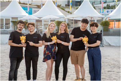 Six people on a beach holding toy figures and smiling.