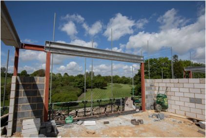 A partially constructed building frame overlooking a grassy landscape under a blue sky.