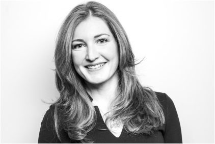 A woman with long hair smiles in a black and white portrait.