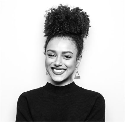 A woman with curly hair smiles brightly in a black and white photo.