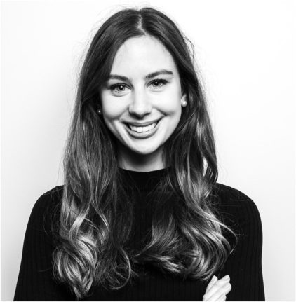 A woman with long hair smiles at the camera in a black and white portrait.