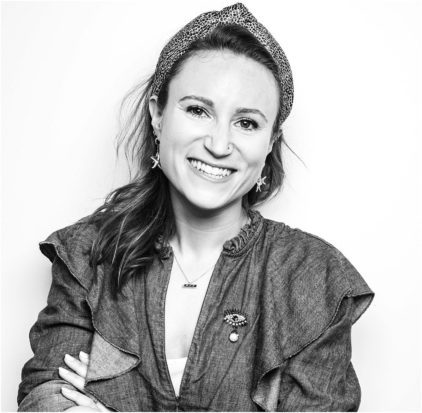 Woman smiling, wearing a headband and earrings, in a black and white portrait.