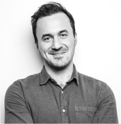 A man smiles warmly in a black and white portrait.