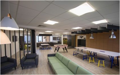 A modern, open-plan office lounge with sofas, tables, and a foosball table.