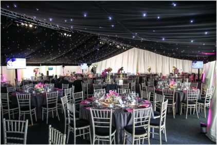 Indoor image of a decorated banquet hall with tables, chairs, and floral centerpieces.