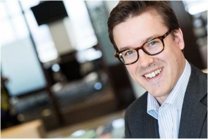 Portrait of a man wearing glasses, indoors, smiling at the camera.