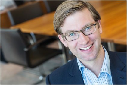 A smiling man in glasses in an indoor portrait.