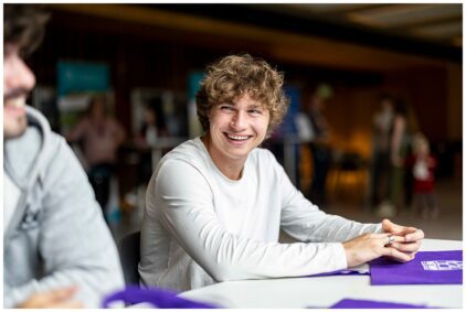 A young man smiling at a table indoors.