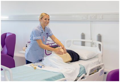 A nurse in uniform practices CPR on a dummy in an indoor hospital setting.