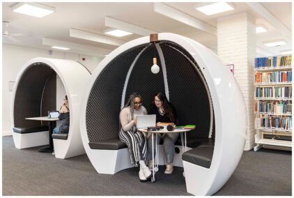 Two people study together in a futuristic pod in a library.