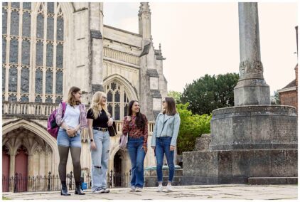 Outdoors image of four people walking and talking near a historic building.