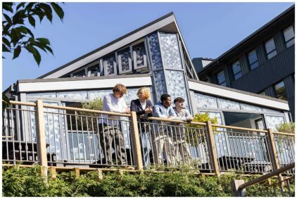 Outdoors image of four people standing on a balcony in front of a modern building.
