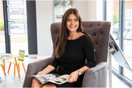 A smiling woman sits in a chair holding a magazine.