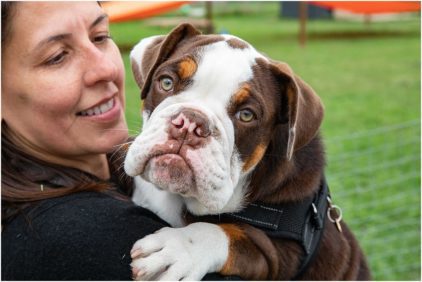 A woman holds a Bulldog puppy outdoors.