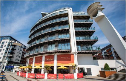 Outdoor image of a modern curved building with a restaurant on the ground floor.