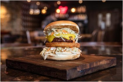 A close-up of a gourmet sandwich with various toppings on a wooden board indoors.
