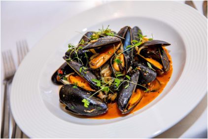 A plate of mussels in a red sauce garnished with herbs, food image.