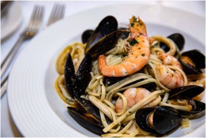 A close-up of a seafood pasta dish with shrimp and mussels, indoors.