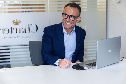 Indoor portrait of a man in a blue suit sitting at a desk with a laptop.
