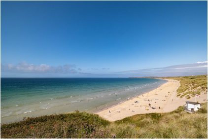 Outdoor landscape of a sunny beach with people enjoying the water and sand.