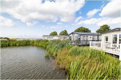 Outdoor landscape of mobile homes beside a pond with lush vegetation.