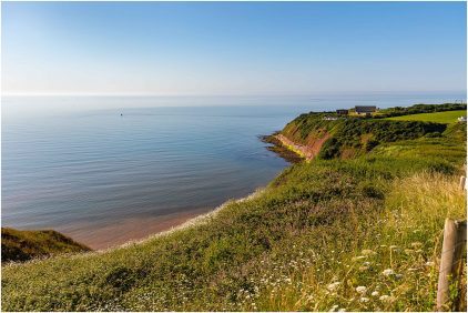 Outdoors image of a coastal landscape with cliffs, sea, and clear blue sky.