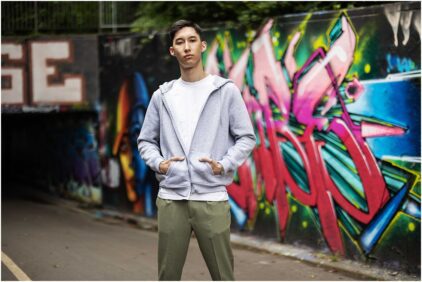 A man in a streetwear outfit stands outdoors in front of vibrant graffiti art.