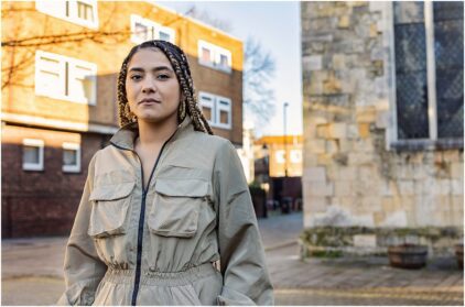 Outdoor portrait of a person with braided hair standing in an urban setting.