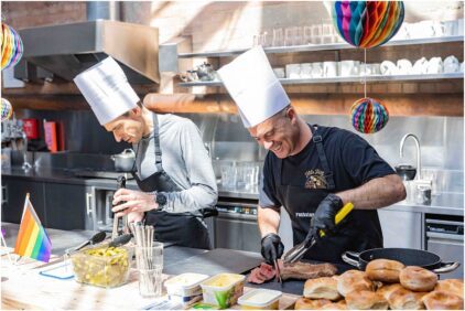 Two chefs in an indoor kitchen preparing food and smiling.