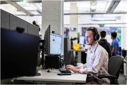 A man wearing headphones works at a computer in an office setting.