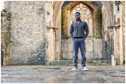 A person standing outdoors in front of a stone archway.