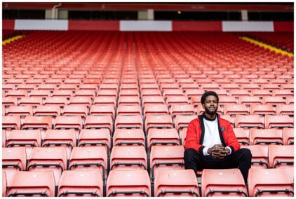 Outdoor image of a person sitting alone in a stadium with rows of red seats.