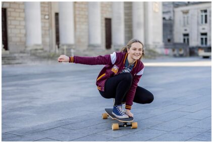 Outdoor image of a person crouching and riding a skateboard on a paved area.