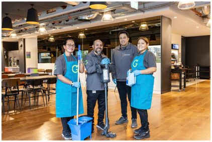 A group portrait of four smiling cleaning staff indoors with equipment in a modern setting.