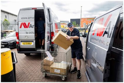An outdoors image of a delivery worker unloading packages from a van into a metal cart.