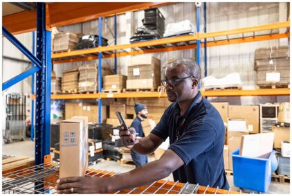 An indoor image of a man scanning a box with a smartphone in a warehouse.