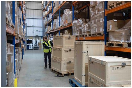 Indoor image of a warehouse worker pushing a cart with wooden crates.