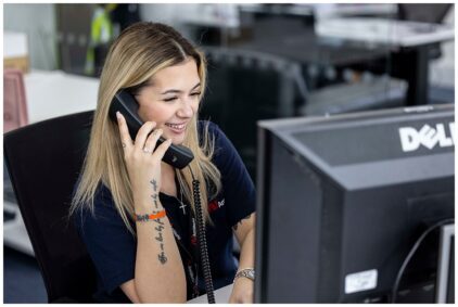 Indoor image of a woman at a desk smiling while talking on the phone.