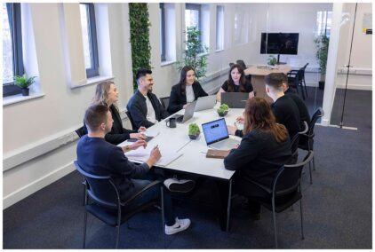 An indoor group meeting around a conference table with laptops and papers.