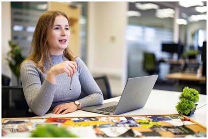 Portrait of a woman sitting at a desk with a laptop in an office setting.