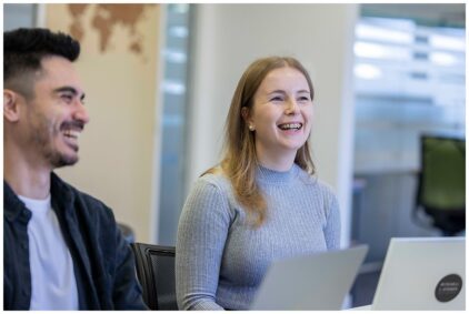 Two people smiling in an indoor office setting with laptops.