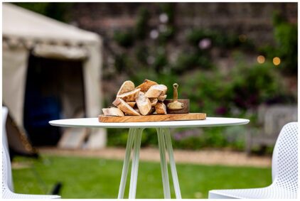 Outdoor image of sliced bread on a wooden tray on a round table.