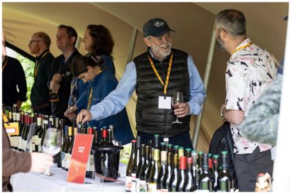 People tasting wine at an indoor event with bottles displayed on a table.