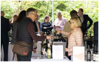An outdoor event with people sampling wine at a tasting table.