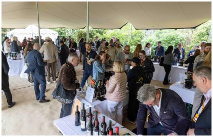Outdoor event with people socializing and tasting wine under a tent.