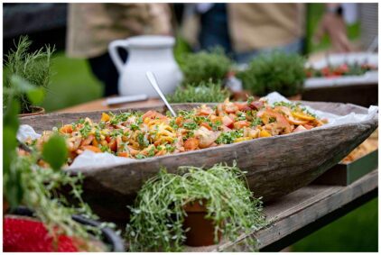 Outdoor image of a colorful salad served in a rustic wooden bowl with greenery around.