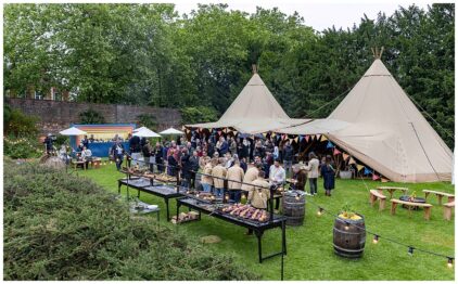 Outdoor event with people mingling near large tents and a food setup.
