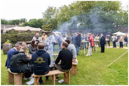 Outdoor event with people socializing and eating on a grassy area.
