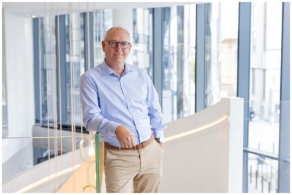 Portrait of a person indoors wearing a light blue shirt and standing in a modern building.